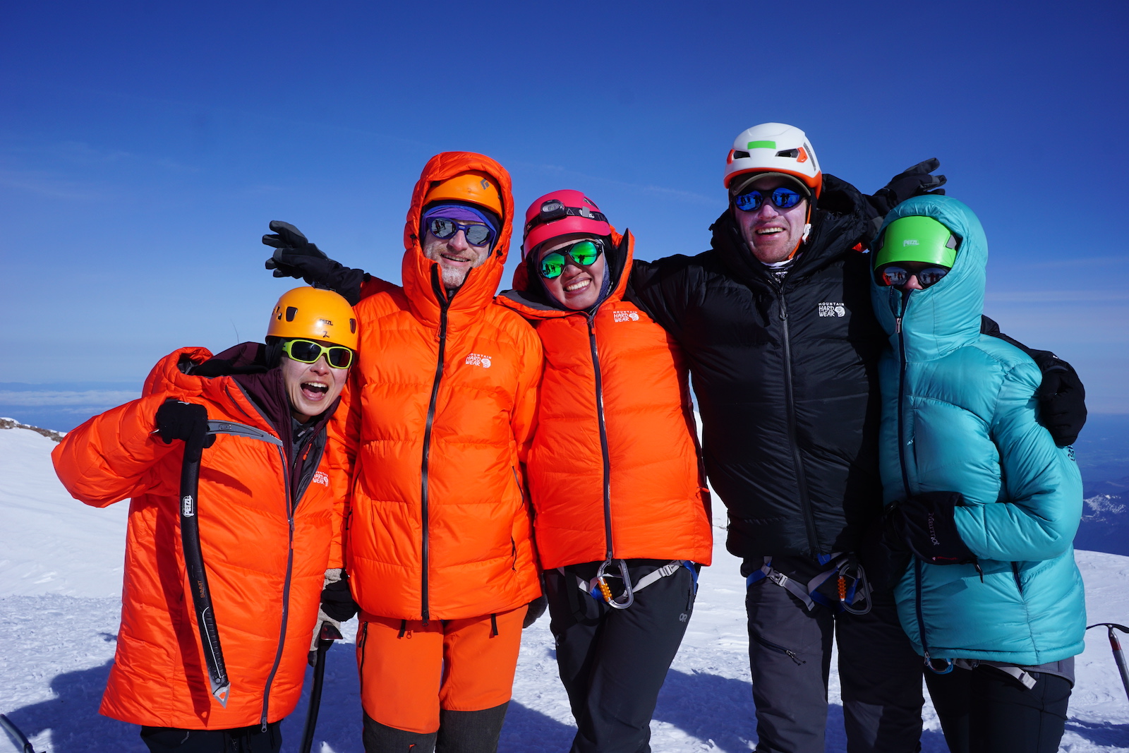Five people standing at the top of Mount Rainier on a clear day bundled up looking happy