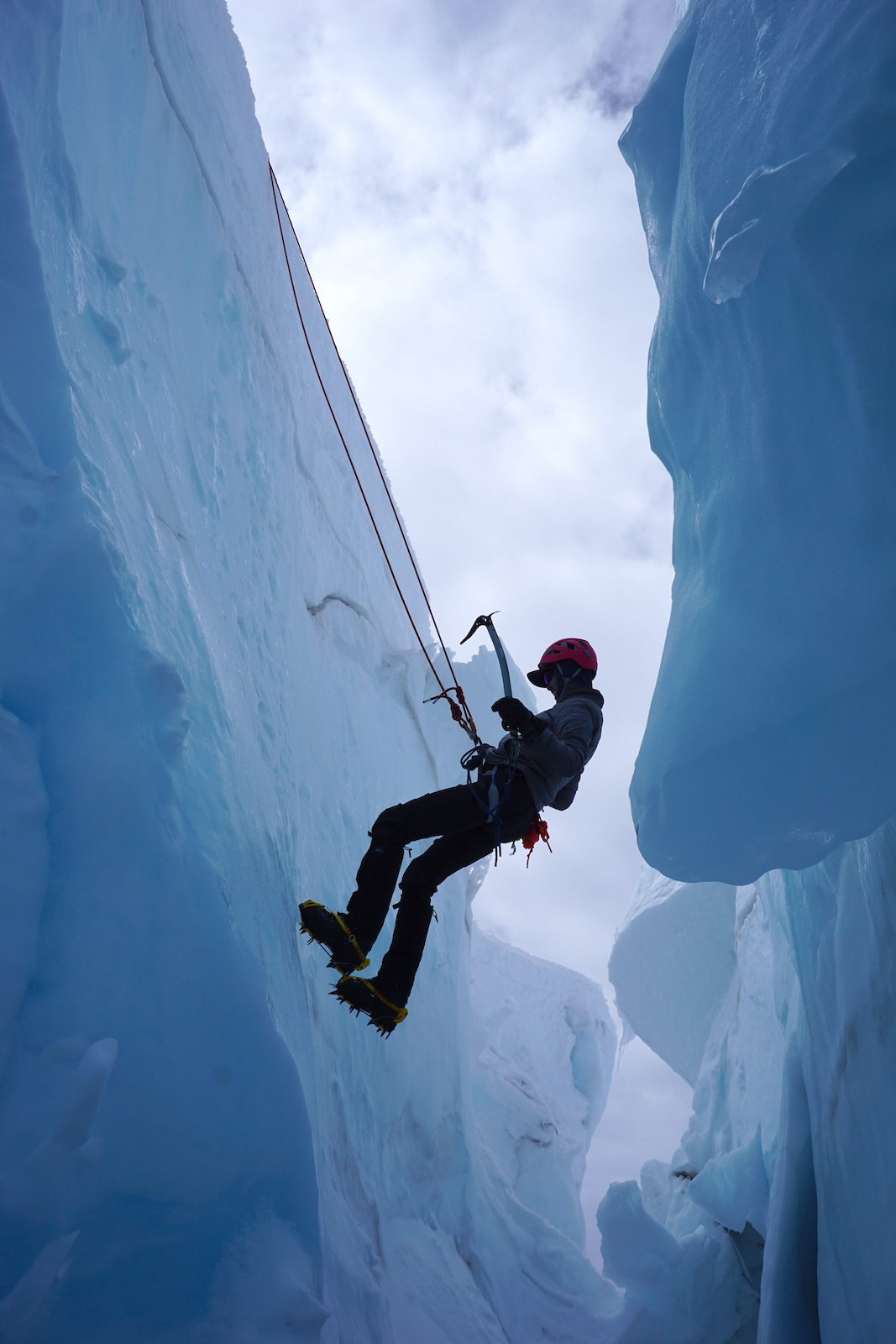 A climber rappels down into a crevasse wearing crampons and holding ice axes