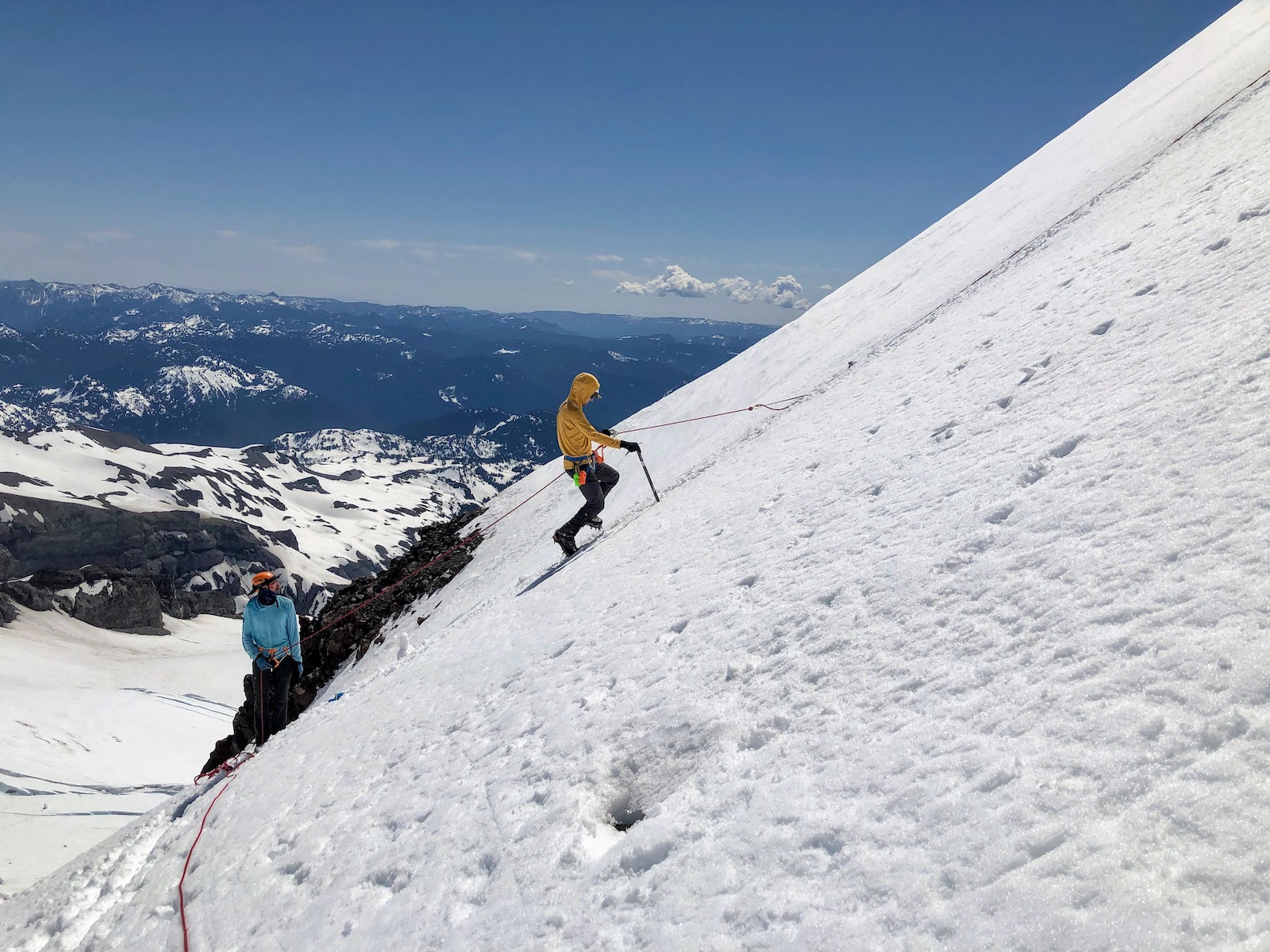 A climber ascending Muir peak from the Cowlitz glacier side on fixed rope with a guide watching from below