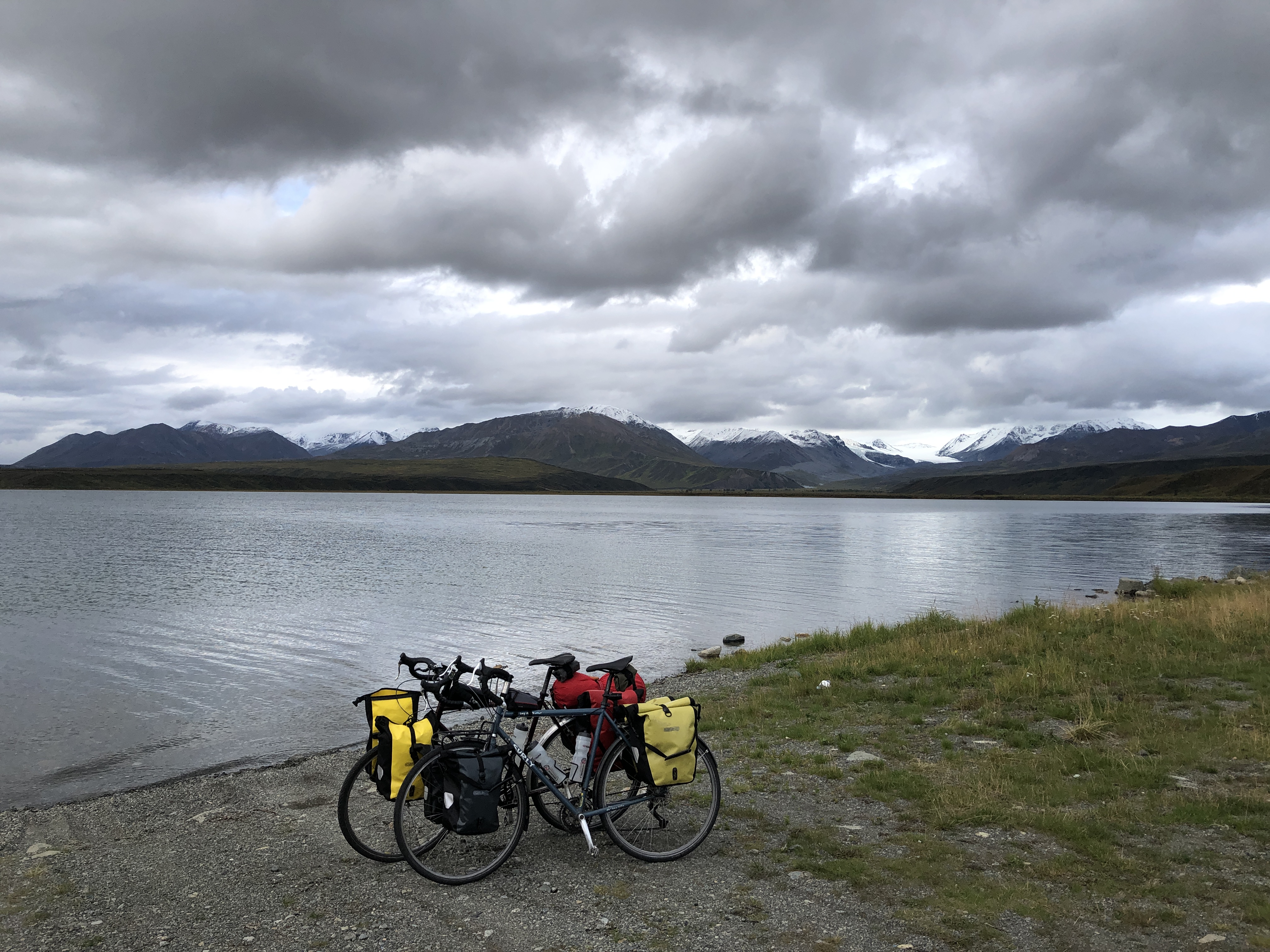 two bikes leaning against each other in front of a lake with mountains and glaciers in the background