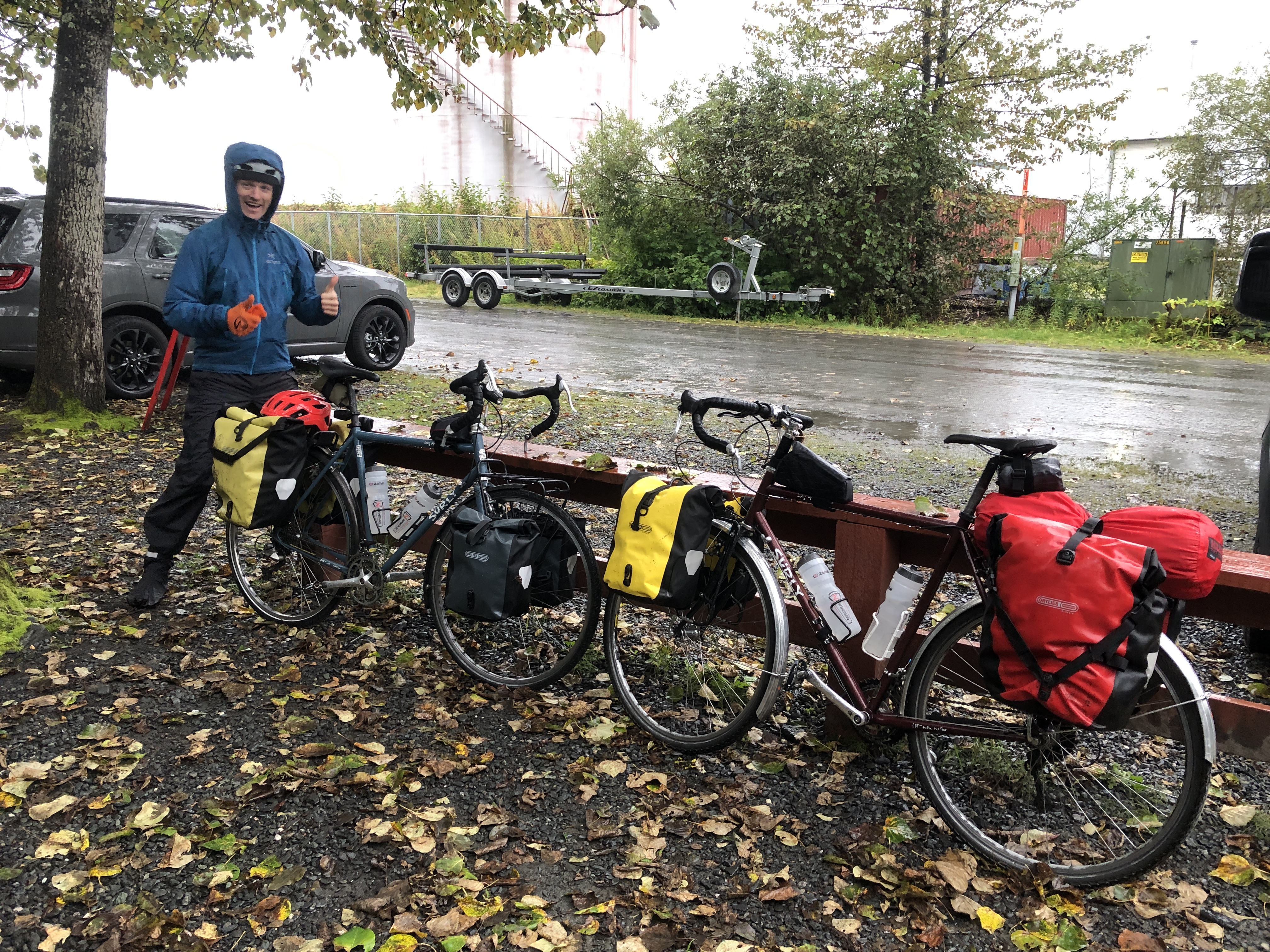 bryan in full rain gear making thumbs up signs by two fully loaded bicycles in the rain