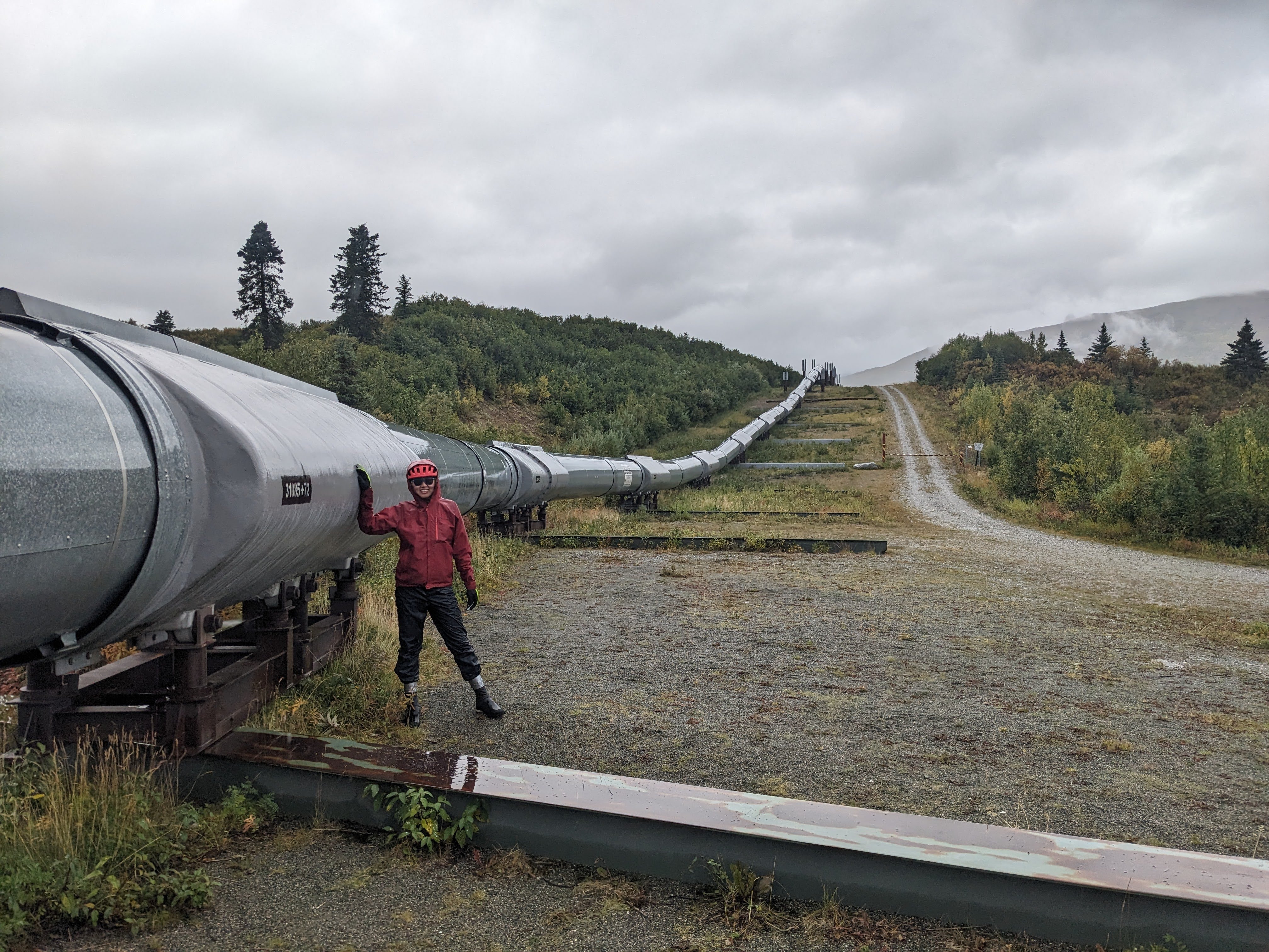 woman in full rain gear standing next to the trans alaska pipeline